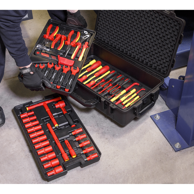 A person is meticulously organizing the Sealey 1000V Insulated Tool Kit 3/8"Sq Drive 50pc - AK7938, which includes pliers, screwdrivers, and sockets in red and yellow, in black plastic cases on a concrete floor for professional use.