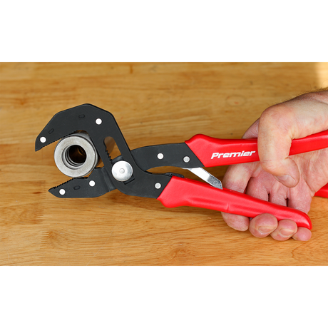 A hand holding Sealey branded multi-grip self-adjusting pliers, model AK8536, with adjustable jaws, gripping a metal bolt against a wooden surface.