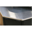 Close-up of a corner of a metallic workbench with "Sealey" label on a dark-colored cabinet, featuring a stainless steel worktop and Model No. APMS19 Stainless Steel Corner Worktop 930mm.