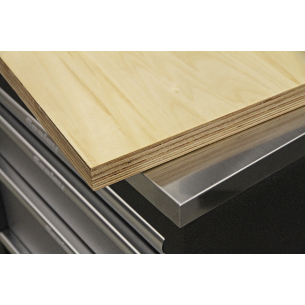 A close-up of a piece of plywood resting on the corner of a Sealey Stainless Steel Corner Worktop 930mm, Model No. APMS19.