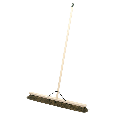 The Sealey Broom 36" (900mm) Stiff/Hard Bristle - BM36H is a large broom with a long wooden handle and stiff bristles. The handle, which includes metal strengthening support, is securely attached to the broom head with a metal bracket, making it suitable for both indoor and outdoor use.