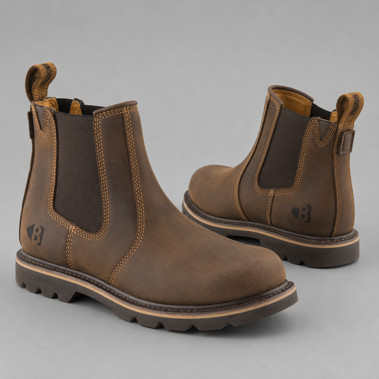 A pair of brown leather Chelsea boots with dark brown elastic side panels and pull tabs, shown on a neutral gray background.