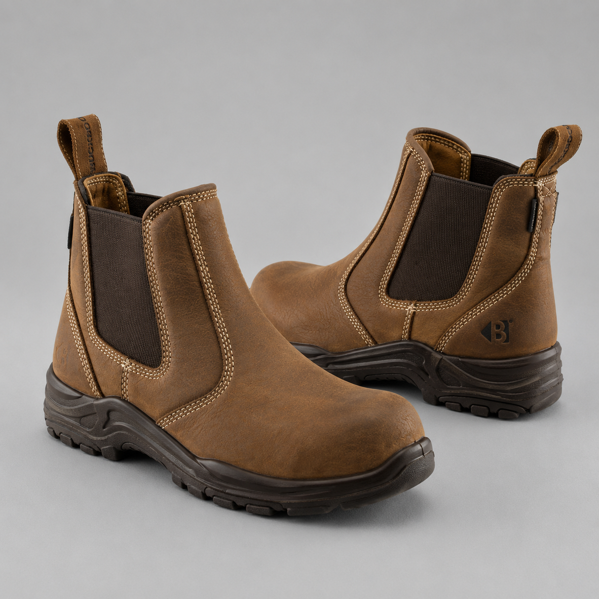 A pair of brown leather Chelsea-style work boots with dark brown elastic side panels and dark soles, shown on a neutral gray background.