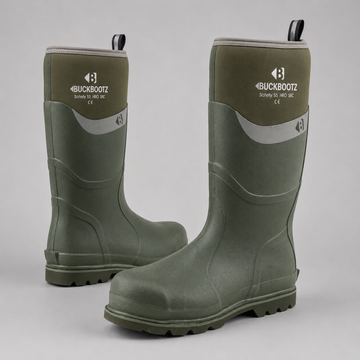 A pair of Buckbootz mid-calf rubber boots in olive green, displayed on a neutral light gray background. One boot is standing upright to show the front branding and side profile, while the other is angled to show the toe and tread.