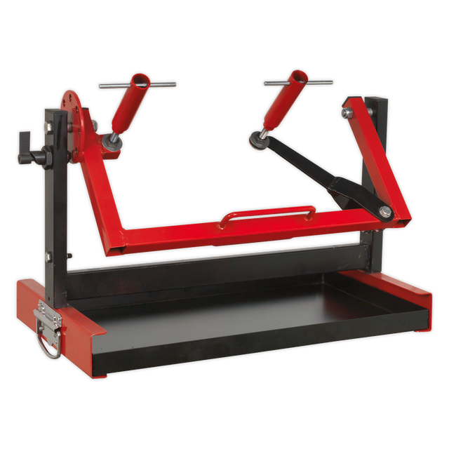 The Sealey Motorcycle Engine Stand - Single/Twin Cylinder - MES01 is a red and black mechanical device featuring adjustable arms, a rectangular base, and an integrated utility tray, designed for securely mounting or holding objects in place.