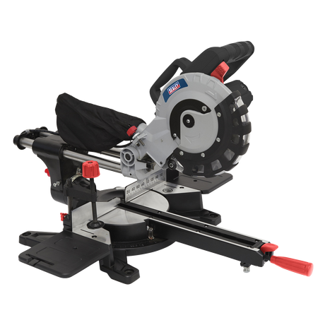 The Sealey Sliding Compound Mitre Saw Ø216mm - SMS216 features a circular TCT blade, sliding rails, and red and black adjustment controls. It includes a dust collection bag, a measurement guide on the base, and a laser guide for precise cuts.