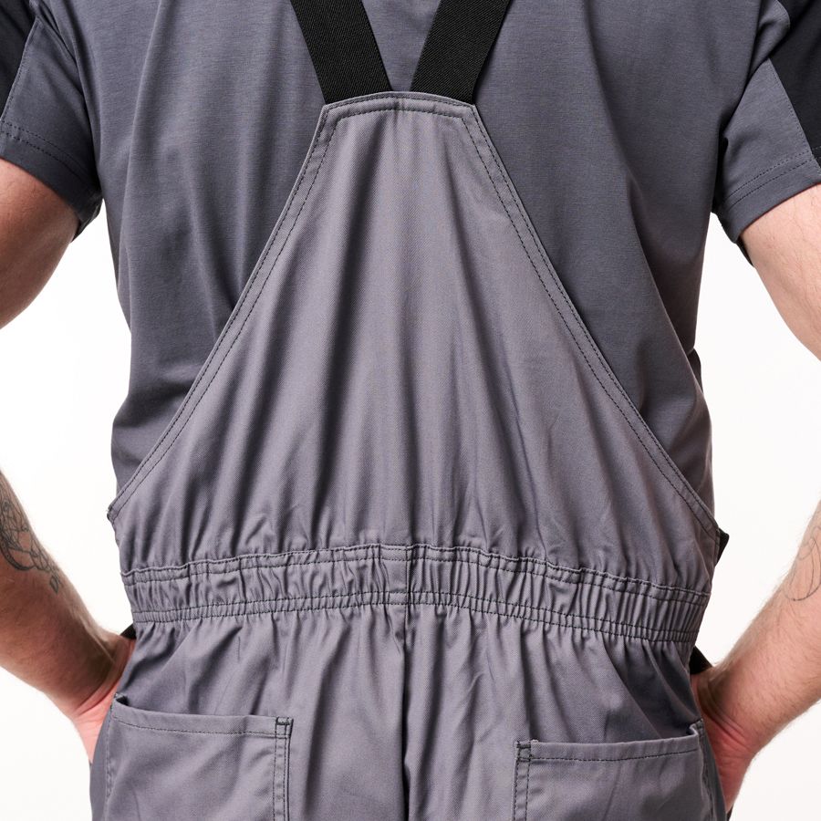 Back view of a person wearing gray bib overalls with black shoulder straps over a dark gray t-shirt, shown against a plain white background.