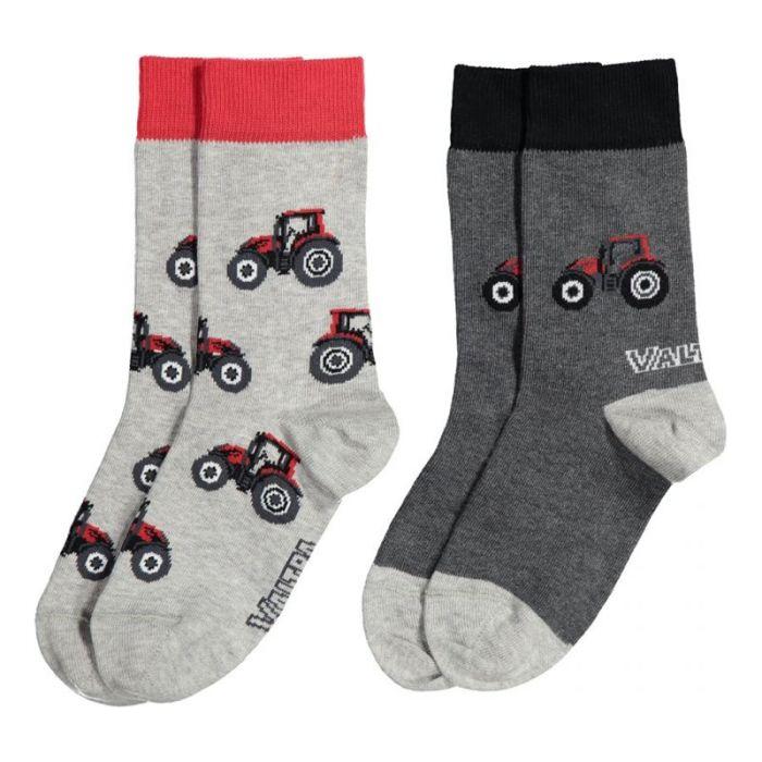 Two pairs of AGCO Valtra children's cotton socks featuring red tractor patterns. The pair on the left is gray with red cuffs, and the pair on the right is dark gray with black cuffs. Both pairs display the brand logo "VAL." Model V4280361.