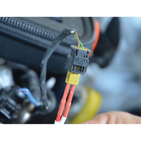 Close-up of a hand holding a small connector with red and white wires attached. The black plastic casing houses the connection leads from the Sparex Diagnostic Test Lead Set - S.151759, ready for automotive diagnostics amidst a bundle of wires in the background.