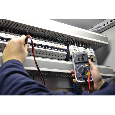 A person uses the Sparex Digital Multimeter - S.151762 to measure DC voltage on an electrical panel, displaying a reading of 232 volts.