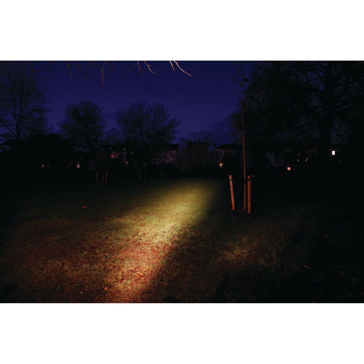A grassy field at night is illuminated by the Sparex Halogen Work Light Square RH & LH - 12V (55W) S.51750, its square shape casting a focused beam, while trees and darkened buildings loom in the background.