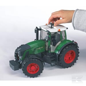 A hand adjusts the top of a Fendt 936 Vario - U03040 by Bruder, featuring green and black colors with red wheels, set against a white background to emphasize its agricultural essence.