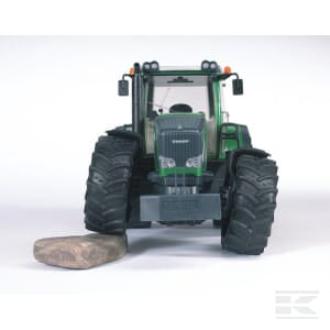 Front view of the green and black Bruder Fendt 936 Vario - U03040 tractor on a white background, with one of its front wheels positioned on a large rock, epitomizing modern agricultural machinery.