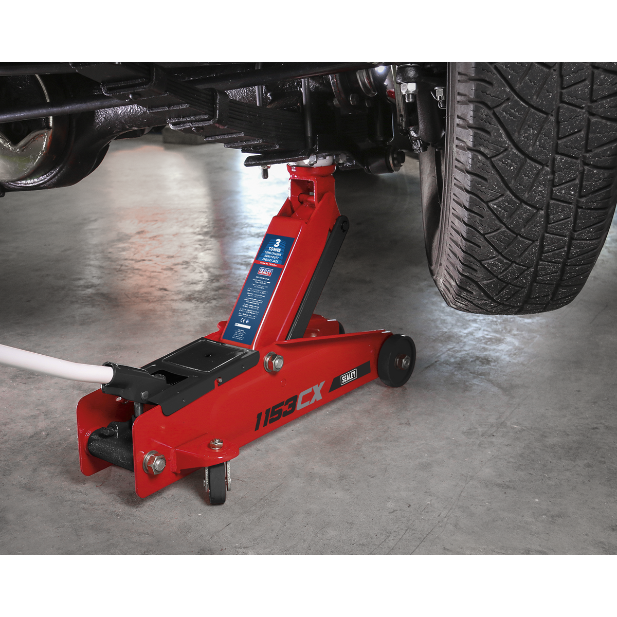 A Sealey Trolley Jack 3 Tonne Long Reach Heavy-Duty (1153CX) lifting a vehicle, showing part of a tire and undercarriage.