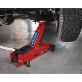 A Sealey Trolley Jack 3 Tonne Long Reach Heavy-Duty (1153CX) lifting a vehicle, showing part of a tire and undercarriage.