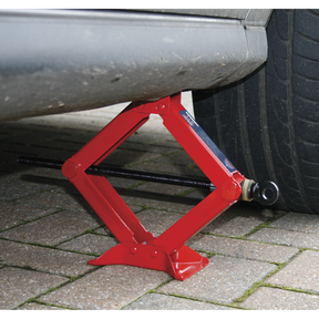 A Sealey Scissor Jack Heavy-Duty 1 Tonne - 57M, featuring a precision thrust bearing, lifts the side of a vehicle near the rear tire on a cobblestone surface, ensuring smooth operation.