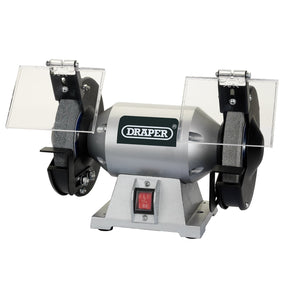 The Draper Bench Grinder, 150mm, 250W - G150C is a compact machine with a silver body labeled "Draper," featuring two grinding wheels, adjustable eye protection shields, and a red on/off switch.