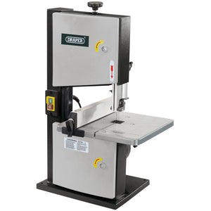 The Draper Bandsaw With Steel Table, 200mm, 250W - BS200B is a compact and metallic saw that flaunts the renowned Draper logo. It offers a cutting capacity suitable for various tasks and features a control panel equipped with a power button, safety warnings, and adjustable components to ensure precise cutting. Additionally, the tilting table feature enhances its versatility for specialized projects.