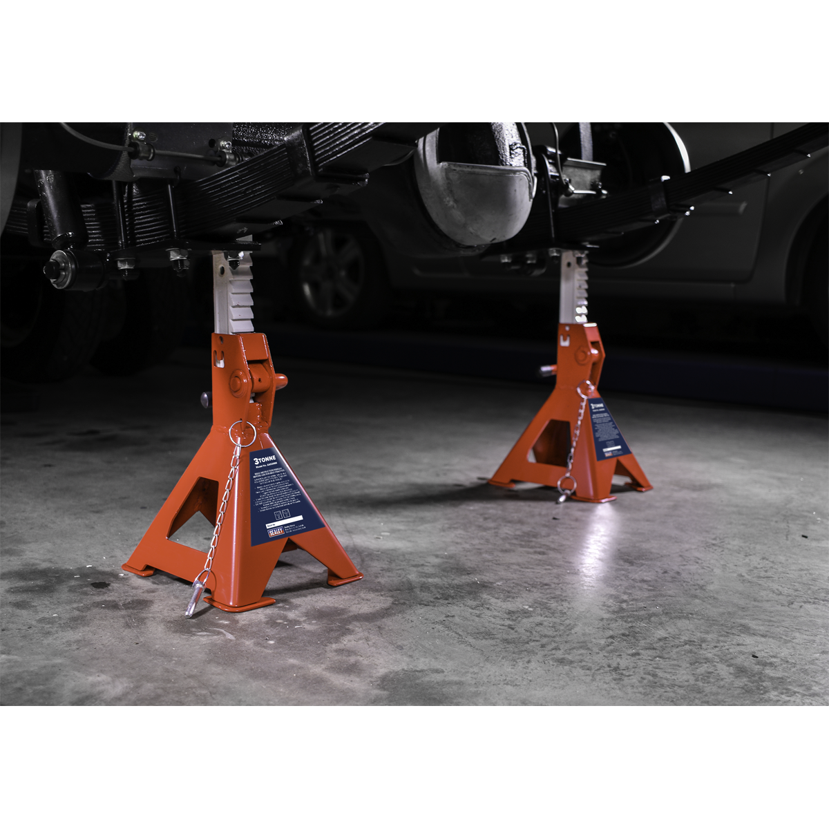 Two Sealey Axle Stands (Pair), model AAS3000, each with a 3-tonne Auto Rise Ratchet capacity and cast iron support posts, supporting a raised vehicle in a garage with a concrete floor.