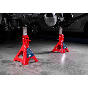 Two Sealey Axle Stands (Pair), model AAS3000, each with a 3-tonne Auto Rise Ratchet capacity and cast iron support posts, supporting a raised vehicle in a garage with a concrete floor.