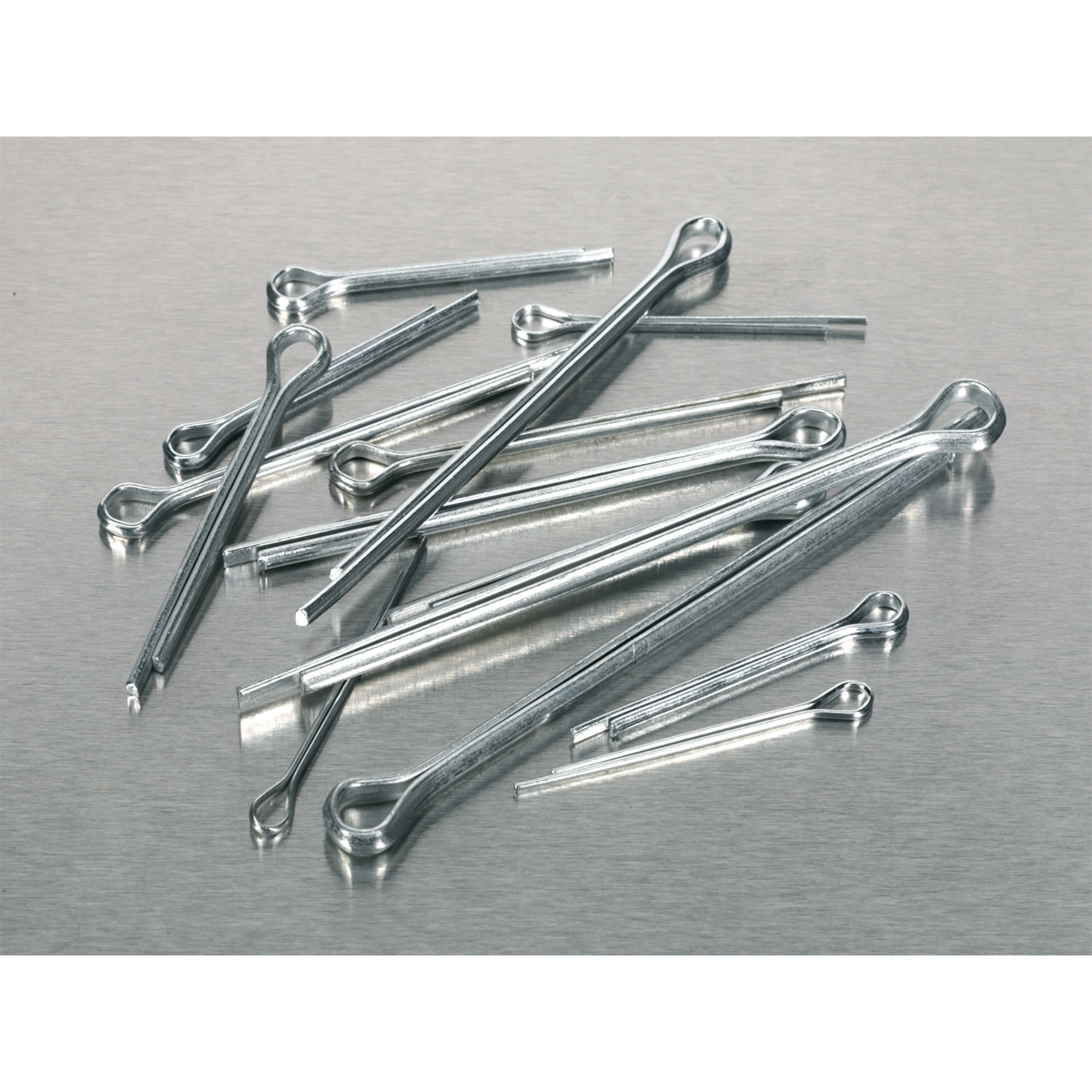 A scattered assortment of Sealey Split Pin Assortment 555pc Small Sizes Metric & Imperial - AB001SP lies on a metallic surface.