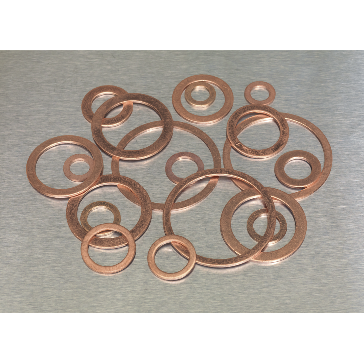 A Sealey Copper Sealing Washer Assortment 250pc - Metric (AB020CW) is scattered on a metal surface.