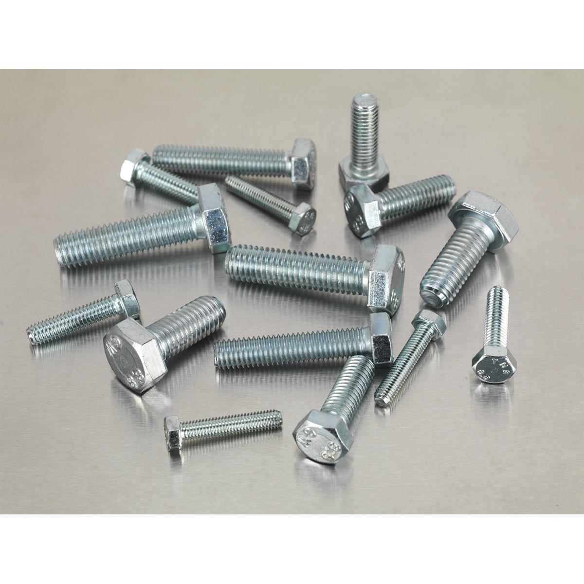 Various sizes of hex bolts, including the comprehensive Sealey Setscrew Assortment 150pc Metric M5-M10 High Tensile - AB048SS adhering to DIN 933 standards, are scattered on a metallic surface, offering an organized yet industrial charm like a partitioned box of tools.