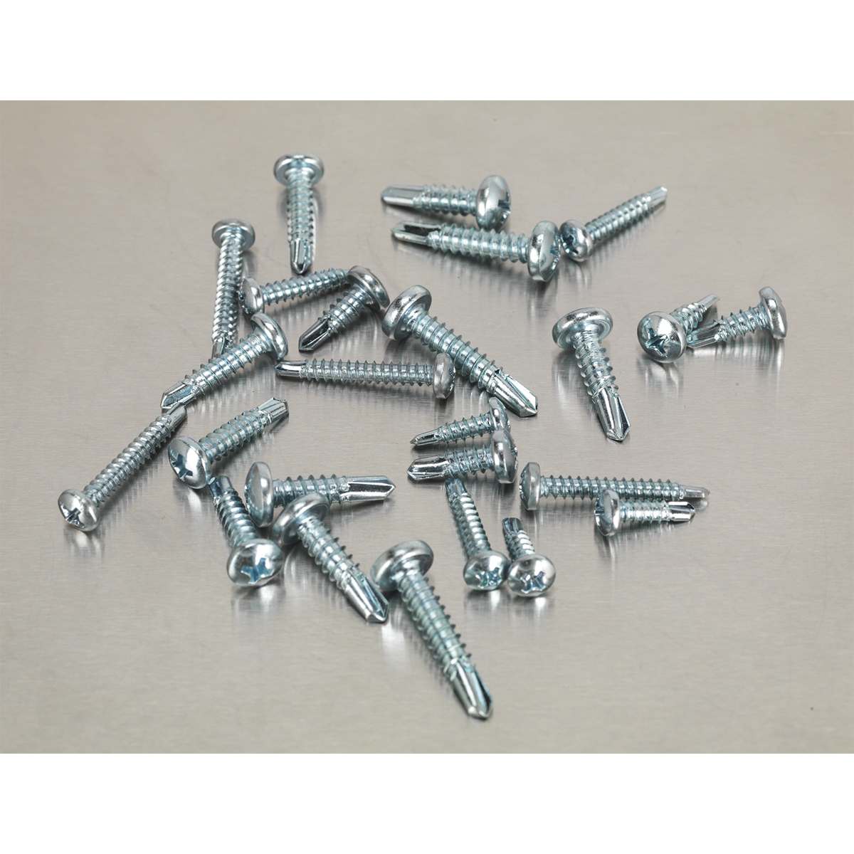 A scattered pile of Sealey's Self-Drilling Screw Assortment 500pc Pan Head Phillips Zinc (AB060SDS) on a light gray surface.