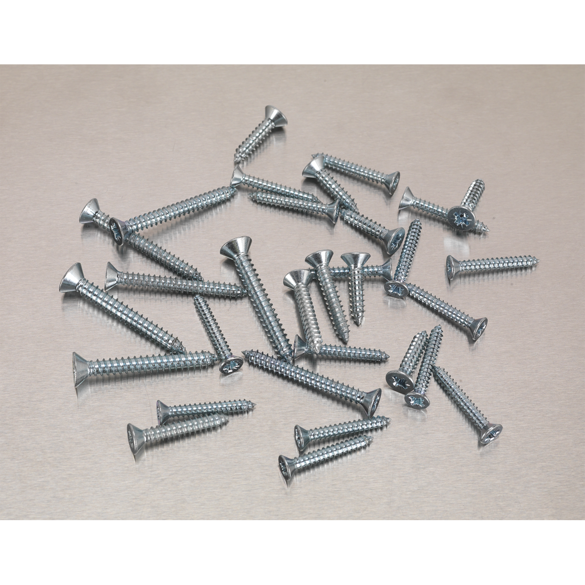 A pile of Sealey Self-Tapping Screws from the DIN 7982 510-piece Countersunk Pozi Zinc Assortment (AB062STCS) of varying lengths scattered on a light gray surface.