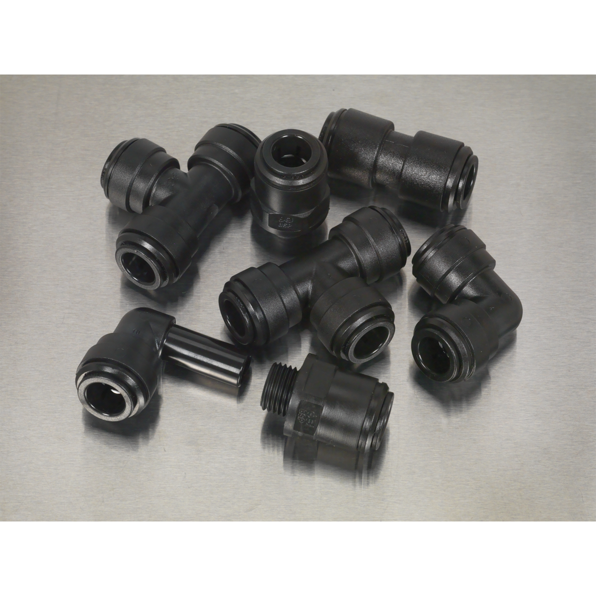 A collection of high-quality components, including the Sealey Speedfit® Coupling Assortment 20pc Ø10mm Metric - AB070JG, featuring black plastic pipe fittings, elbows, straight connectors, and pneumatic couplings, arranged on a gray surface.