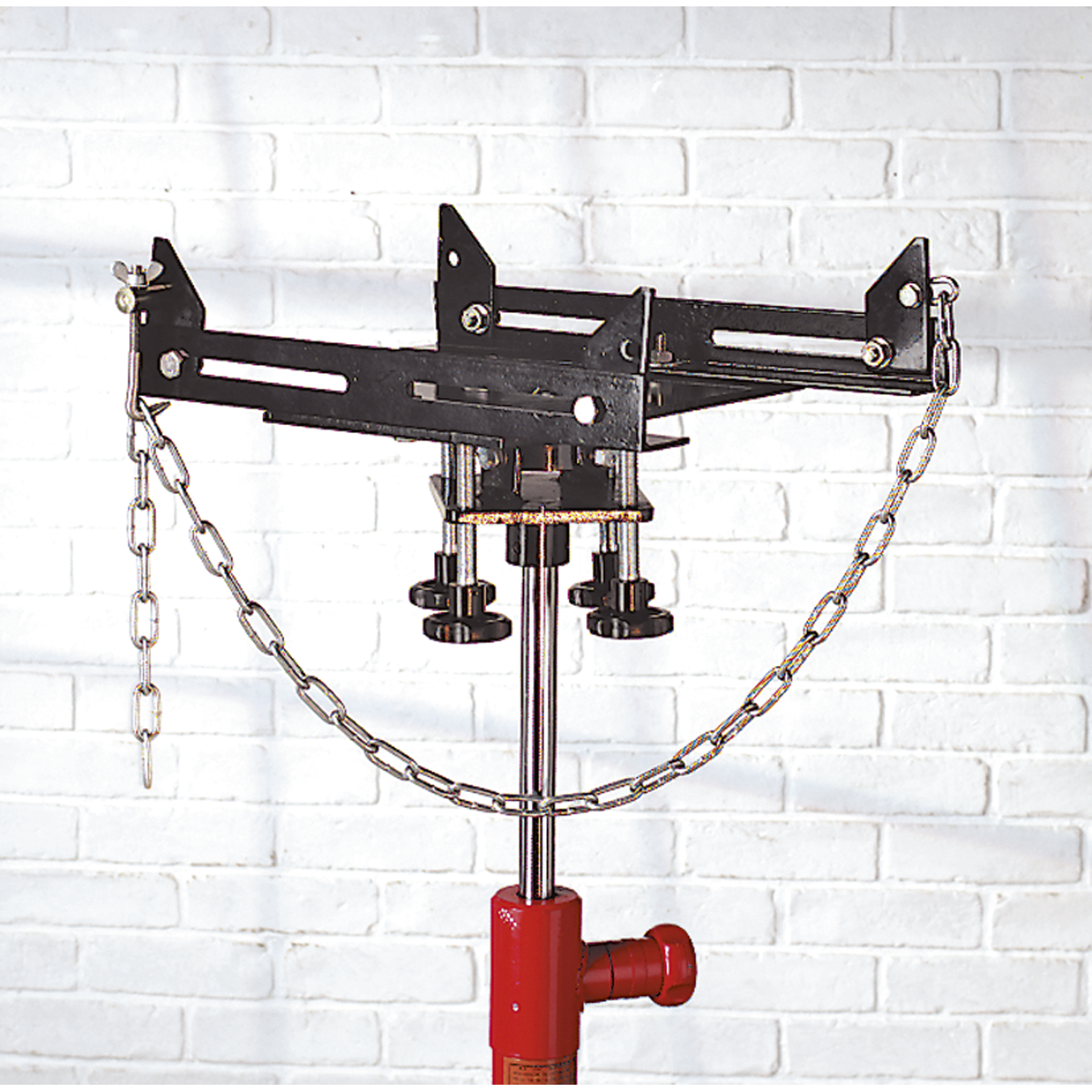 A Sealey Adjustable Gearbox Support 500kg Capacity for 300TR, 300TRQ, 600TR, 600TRQ (ADT3), featuring adjustable supports and chains on a metal stand, set against a white brick wall.