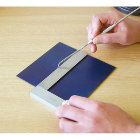 A person uses the Sealey Precision Steel Square 150mm - AK11150 to examine a blue material resting on a flat surface, alongside a metal ruler.