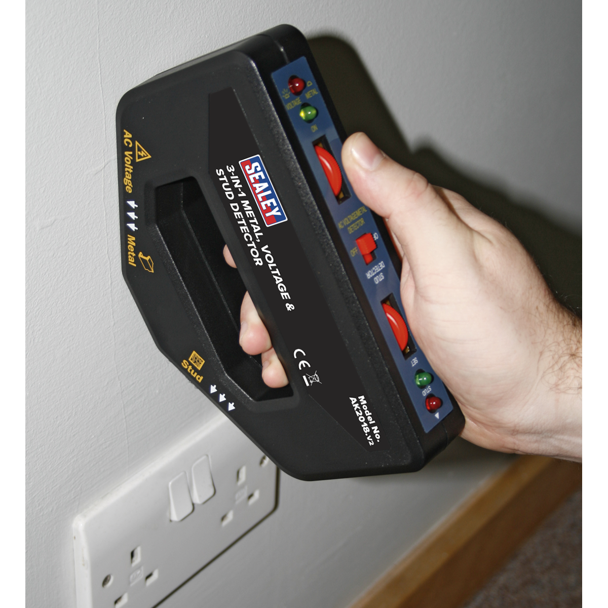 A person holding a Sealey AK2018 Metal, Voltage & Stud Detector 3-in-1 near a wall socket, ready to identify wooden studs with this essential hand tool.