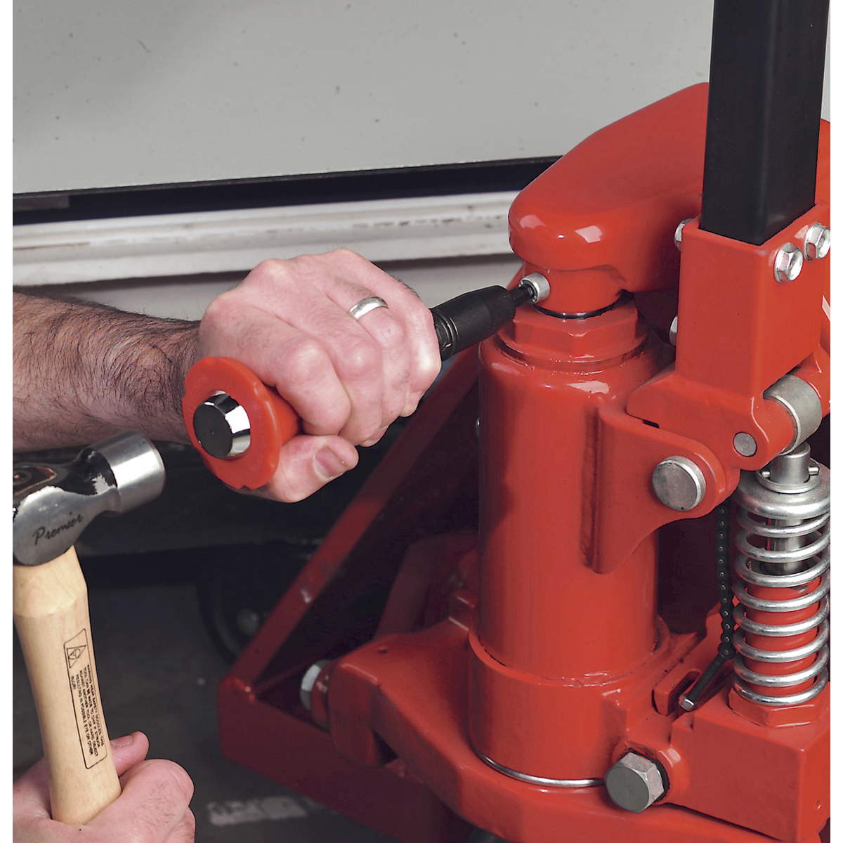 Close-up of a person's hands using a Sealey AK2081 Impact Driver Set 15pc Protection Grip and a 1/2"Sq drive impact driver on a red hydraulic floor jack.