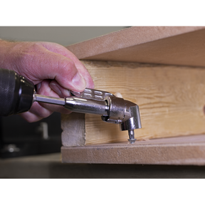 A person uses the Sealey Angle Driver - AK2104 on a power drill with magnetic bit retention to drive a screw into a corner of a piece of wood.