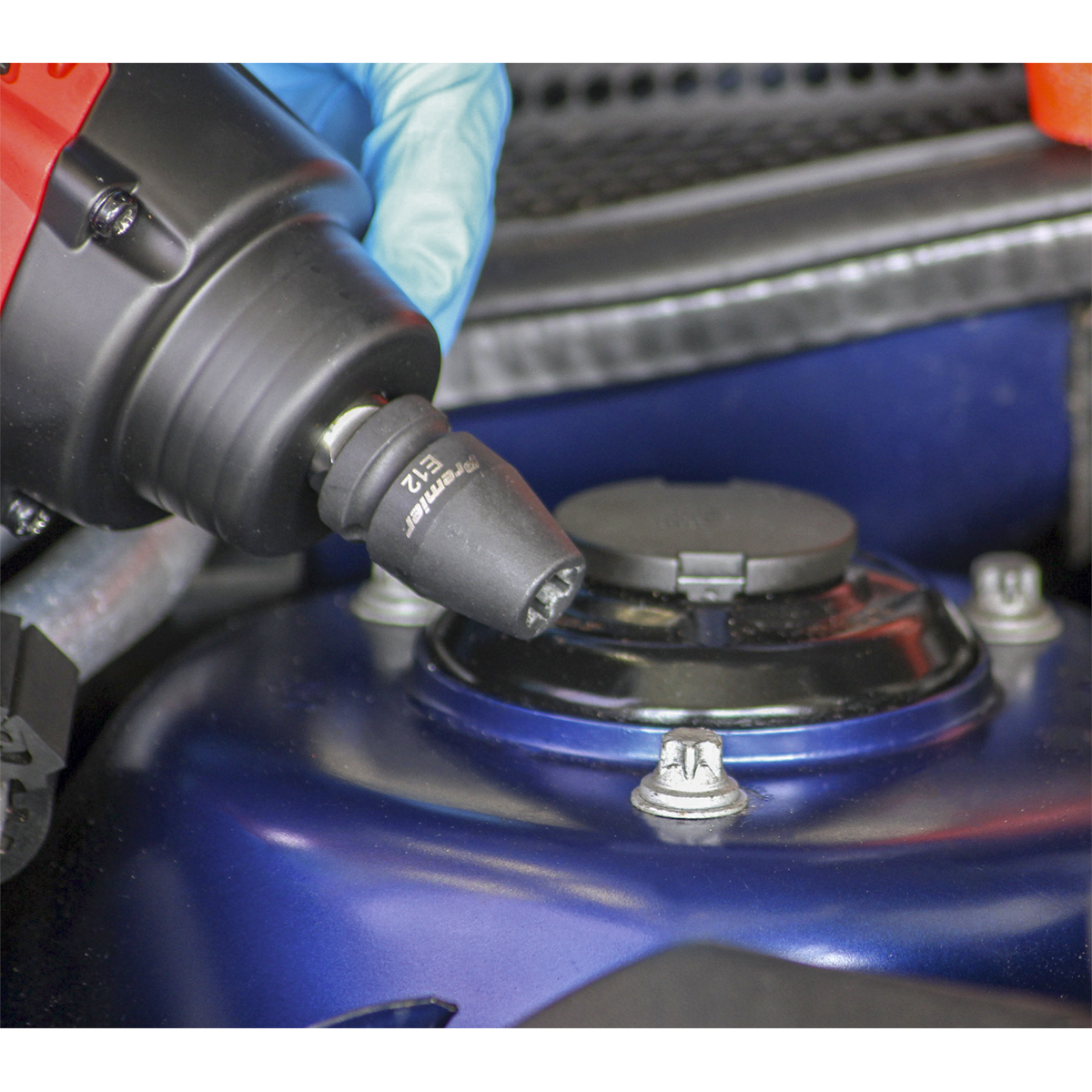 Close-up of a person wearing a blue glove using a Sealey Impact TRX-Star* Female Socket Set 10pc 1/2"Sq Drive (AK2301) with an electric wrench to tighten a bolt on a blue automotive part.