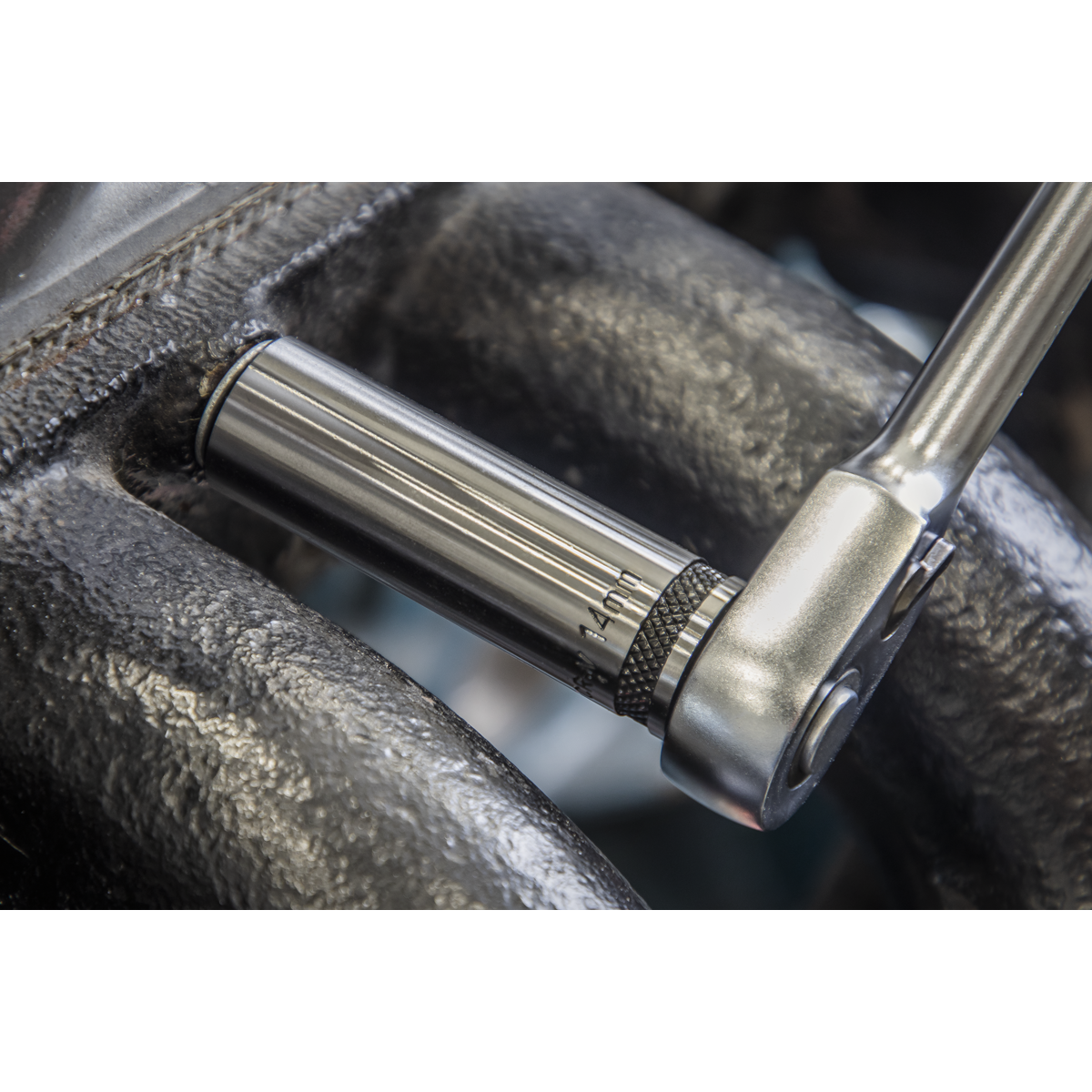 A close-up of a ratchet wrench from Sealey's Socket Set 13pc 1/2"Sq Drive Deep Lock-On™ 6pt Metric - Black Series (AK2745B) being used to tighten a shiny metal bolt on a machine part with a dark, textured surface. The wrench's polished black chrome finish gleams, ensuring both style and durability with its Chrome Vanadium steel construction.