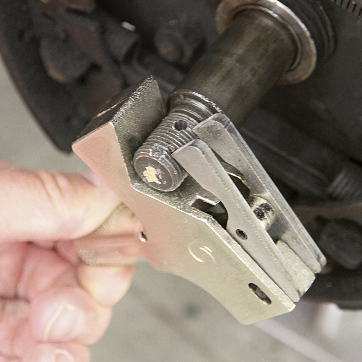 A close-up of a person's hand using the Sealey Adjustable Thread Restorer M4-M45 - AK314 to restore damaged threads on a metal component, possibly part of machinery or a vehicle.