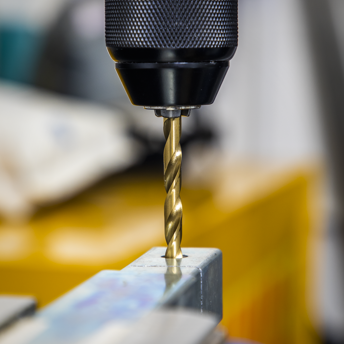 A close-up view of a Sealey Drill & Bit Accessory Set 35pc - AK3735, featuring a drill bit attached to a stainless steel bit holder as it makes a hole in a piece of metal.