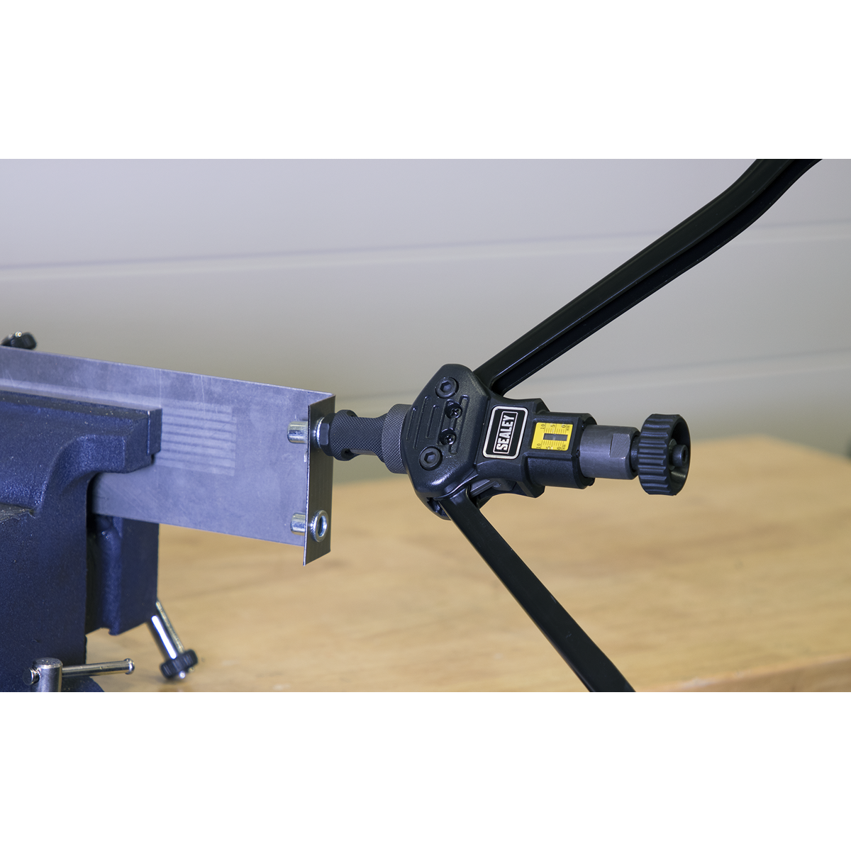 The Sealey Long-Arm Threaded Nut Riveter - AK3985, secured in a bench vice, is precisely cutting a rectangular piece of metal, aided by its adjustable stroke scale.