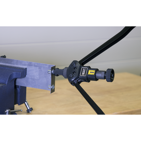 The Sealey Long-Arm Threaded Nut Riveter - AK3985, secured in a bench vice, is precisely cutting a rectangular piece of metal, aided by its adjustable stroke scale.