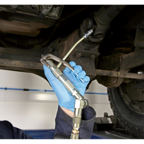 A person wearing blue gloves uses the Sealey Grease Pump Air Operated 50kg - AK453X connected to a grease hose to lubricate a component underneath a vehicle.