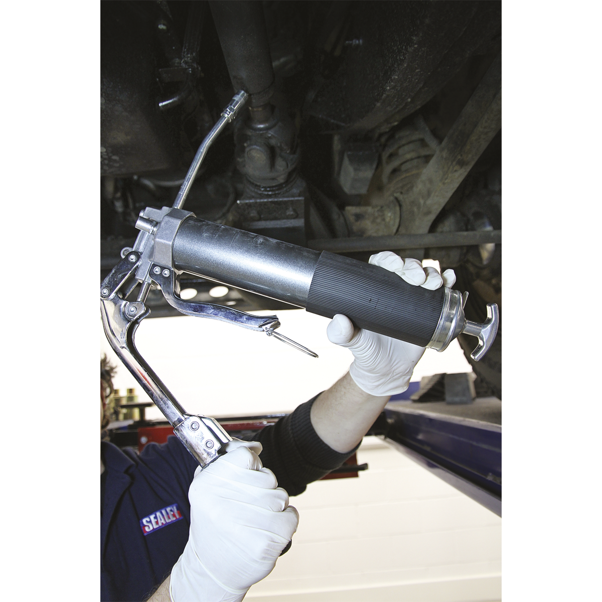 A person in white gloves uses the Sealey Grease Gun 2-Way Operating 3-Way Fill Heavy-Duty - AK48 to lubricate a machinery component.