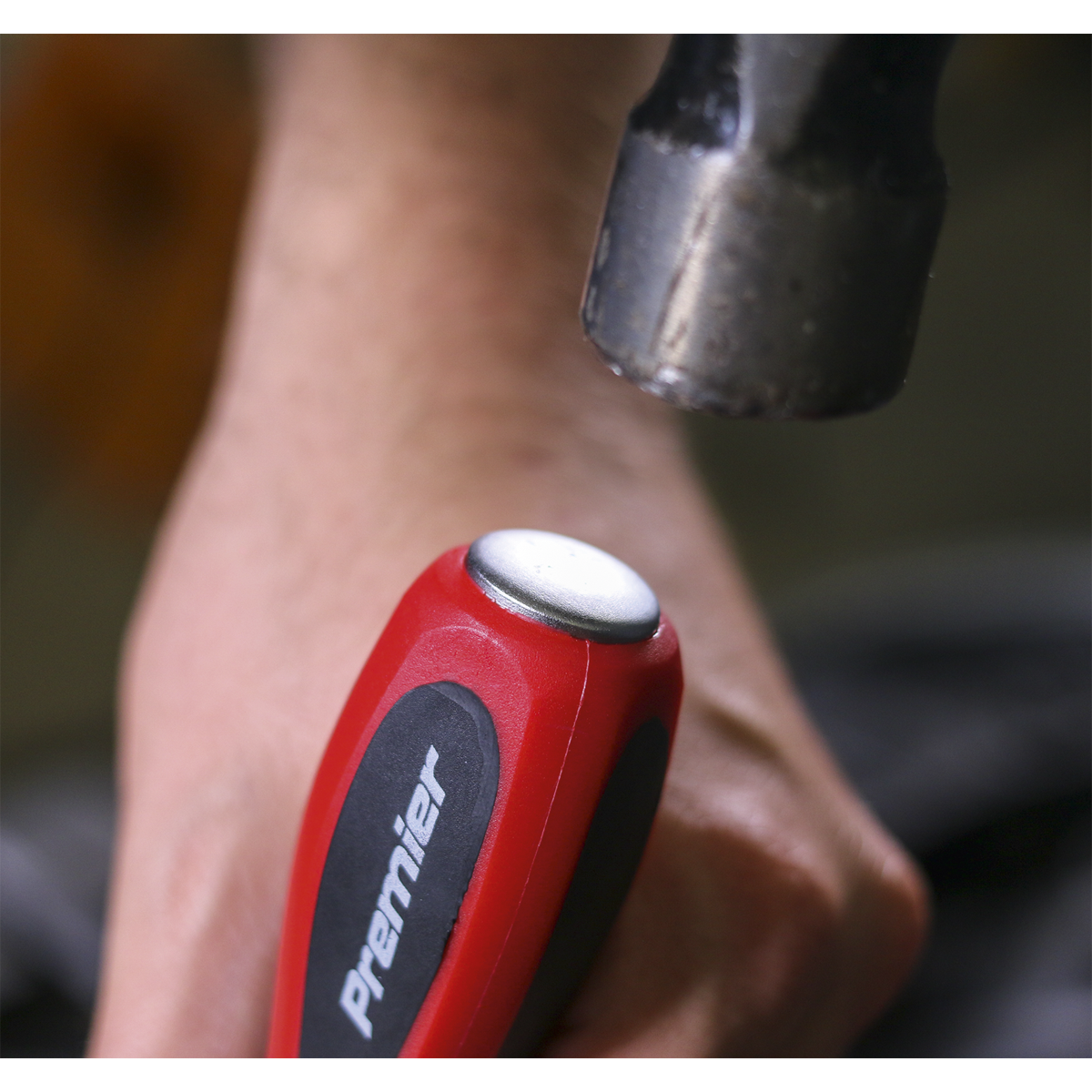 Close-up of a hand holding a red-handled screwdriver from the Sealey Screwdriver Set 6pc Hammer-Thru - AK4932, featuring a metal cap and Chrome Vanadium steel construction, with a hammer poised above it, indicating impact; this high-quality tool is supported by Sealey's lifetime guarantee.