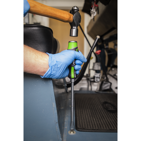 A person wearing blue gloves grips a soft-handled Premier Hand Tool from the Sealey Hammer-Thru Screwdriver Set Hi-Vis Green 6pc - AK4940HV against a metal surface while striking it with a hammer.