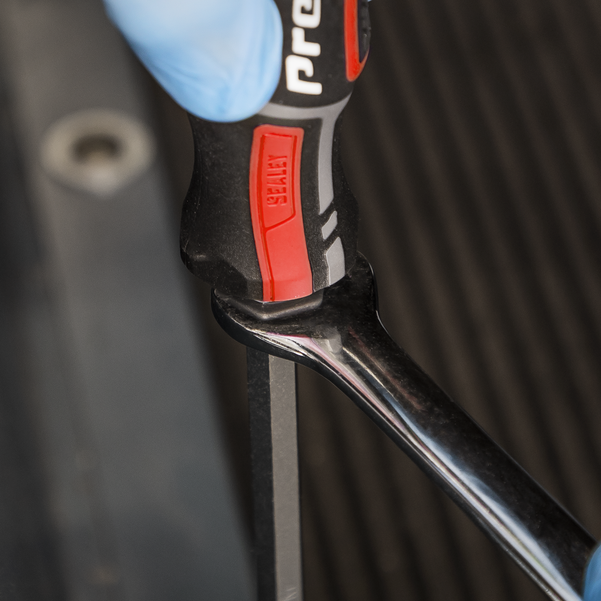 Close-up of a gloved hand holding a Sealey Hammer-Thru Screwdriver from the AK4941 9pc set, turned vertically against a blurred background.