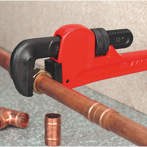 A Sealey Pipe Wrench European Pattern 250mm Cast Steel - AK5102, featuring high-strength, drop-forged carbon steel jaws, is being used to tighten a brass fitting on a copper pipe. Other pieces of copper piping are scattered on a gray surface. Trust in the reliability of Sealey Hand Tools, which come with a lifetime guarantee.