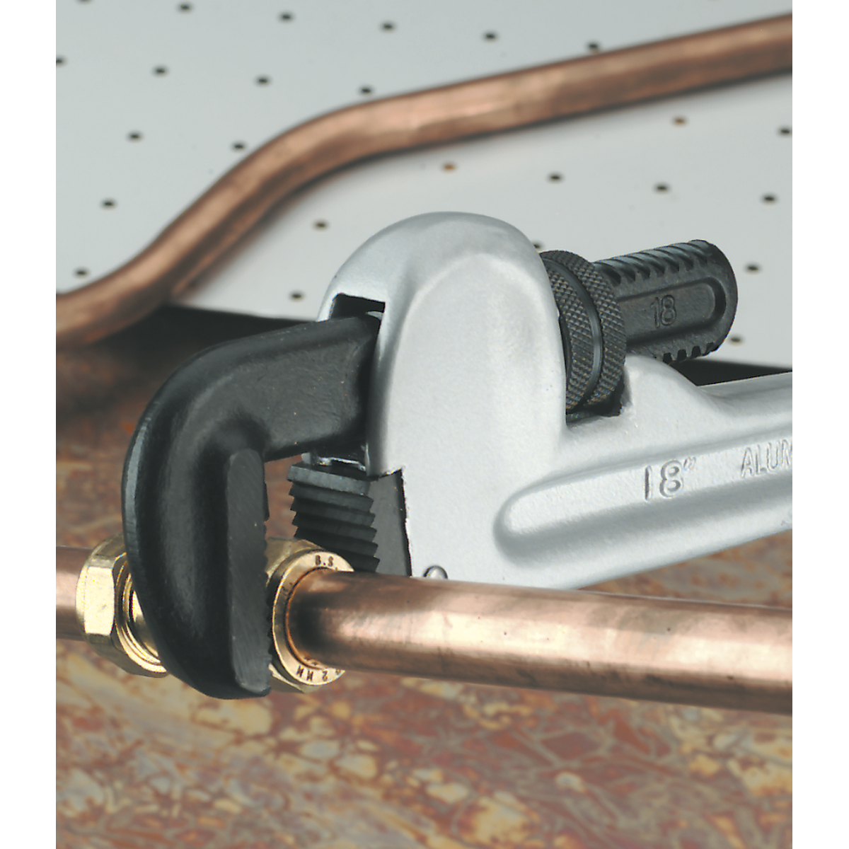 A Sealey Pipe Wrench European Pattern 610mm Aluminium Alloy (AK5110) is gripping a copper pipe with a brass fitting, set against a pegboard background.