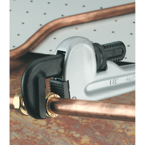 A Sealey Pipe Wrench European Pattern 300mm Aluminium Alloy - AK5107 adjusts a copper pipe against a background with a white pegboard.