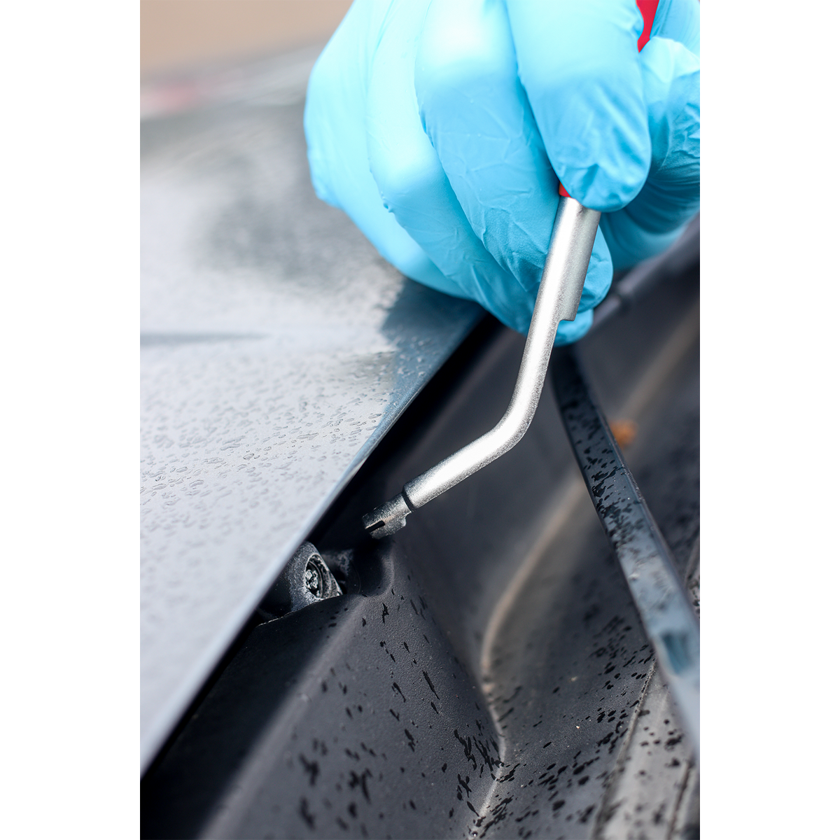 A person wearing blue gloves uses the Sealey Washer Jet Tool - Vauxhall/Opel - AK52207 to tighten a bolt on a wet metal surface.